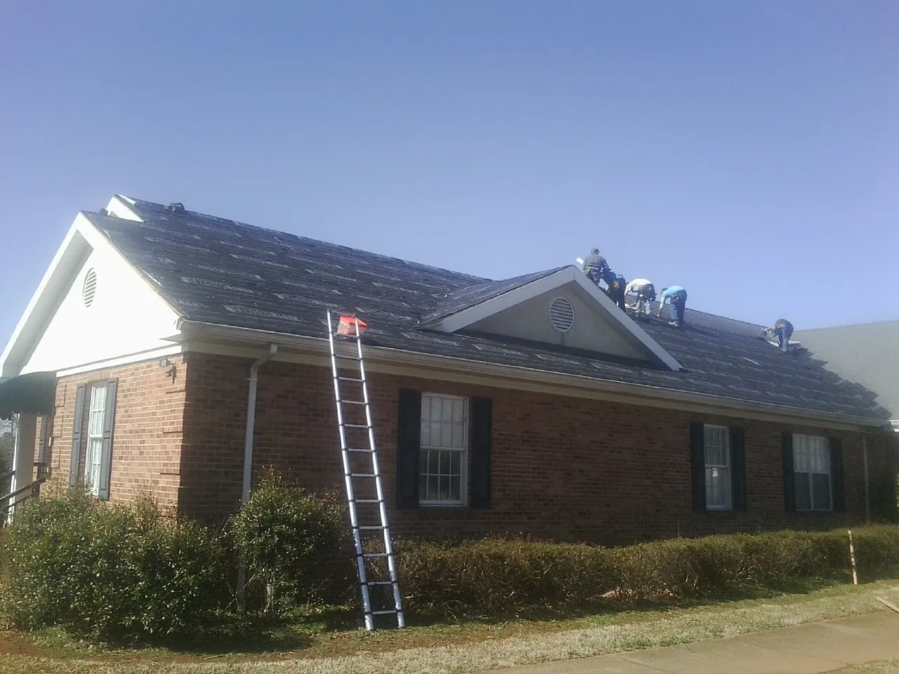 Crew tearing shingles off a brick ranch roof with a ladder set — Emergency Roof Repair work by our crew in Owings
