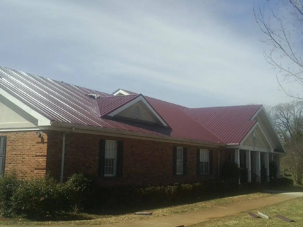 Red metal roof with gabled entries on a long brick building, from a Hail Damage Roof Repair job in Owings