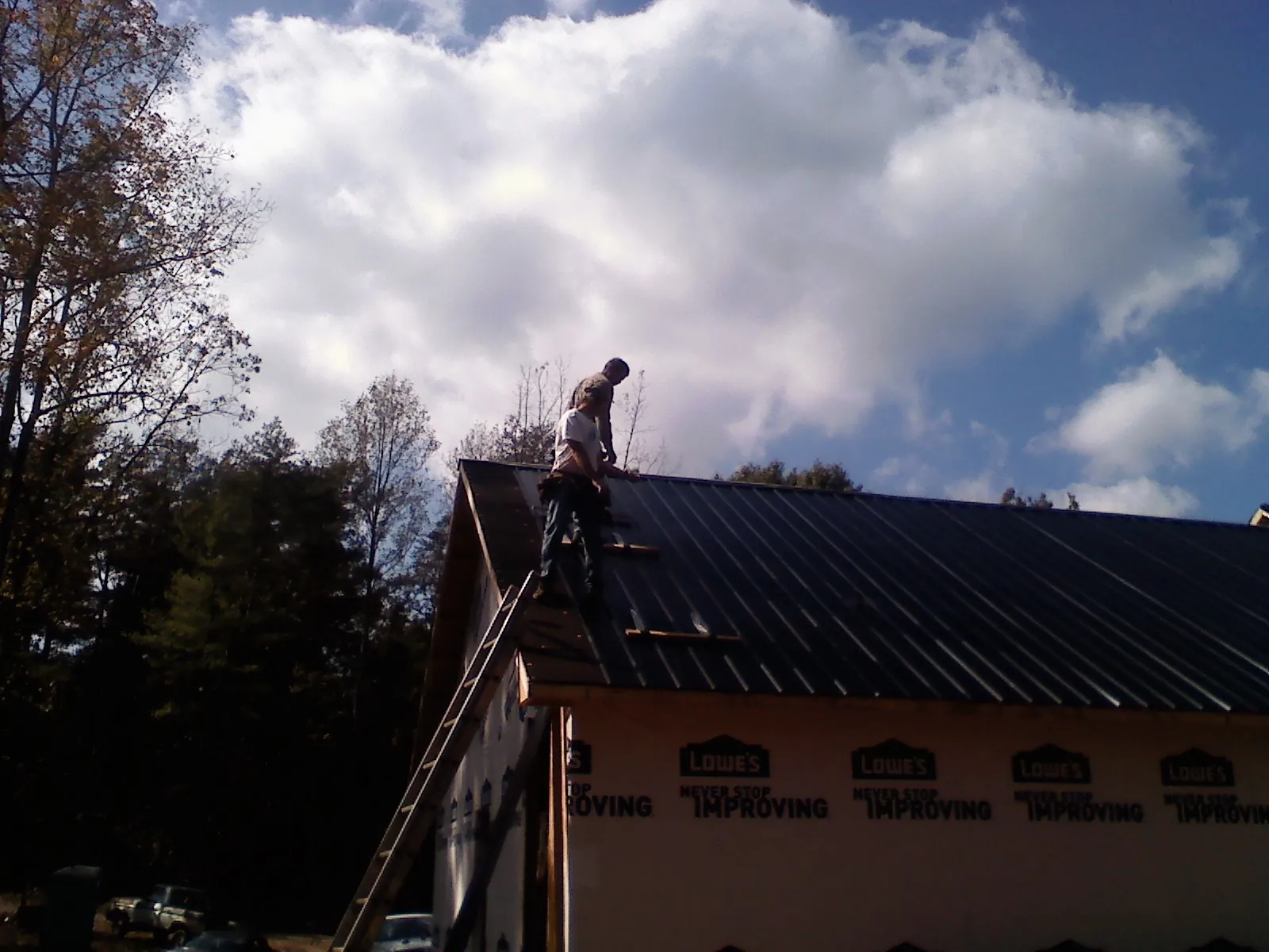 Roofer fastening dark metal panels high against a cloudy sky, from a Roof Inspection job in Owings