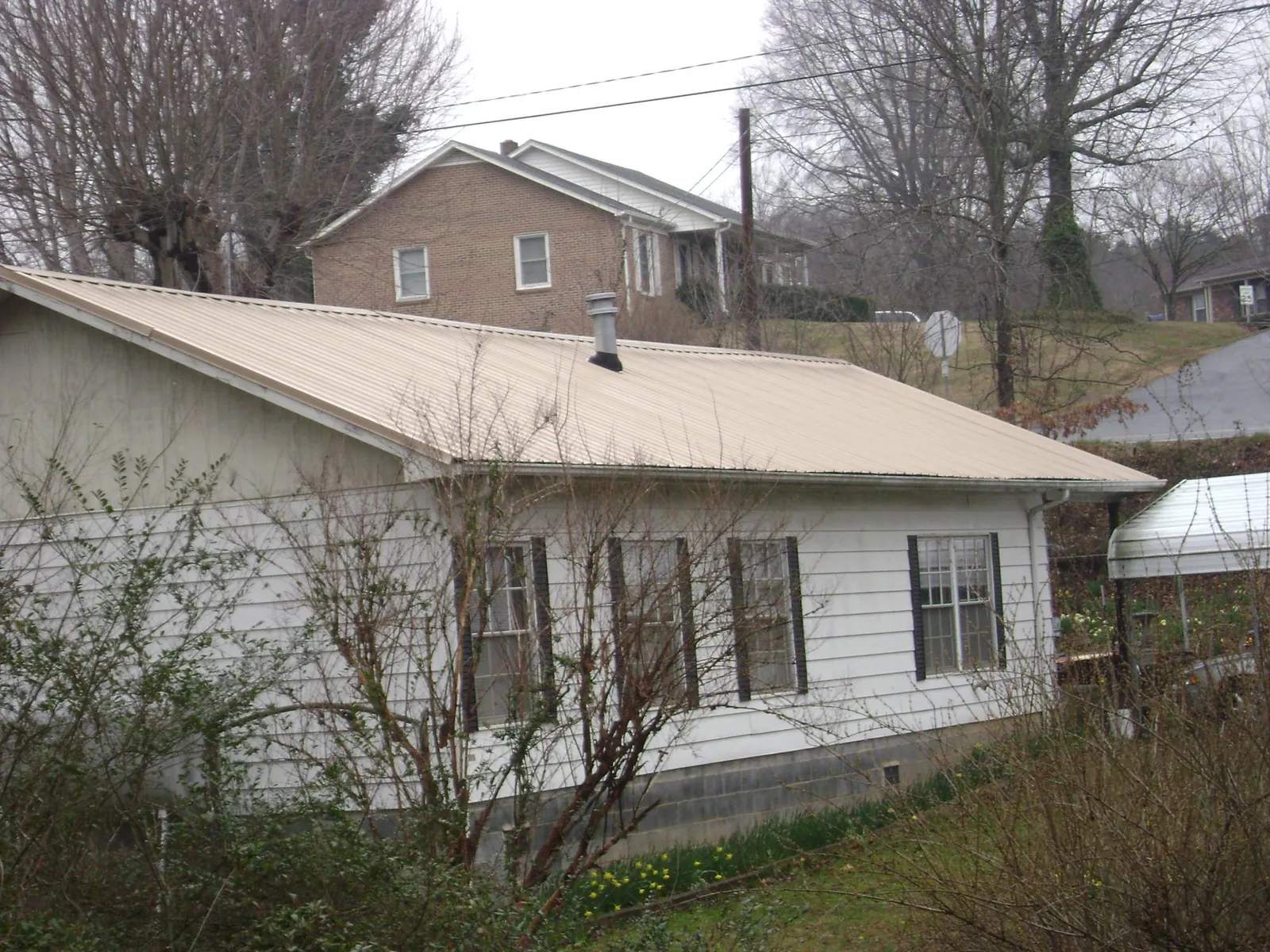 Tan metal roof on a white sided house set into a hillside — Commercial Roofing by Roofing Brothers in Owings
